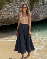 niffty high waisted indigo denim midi skirt with structured pleats worn by a woman on a beach