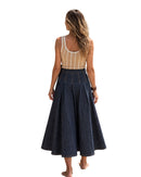 A woman wearing a niffty high-waisted pleated indigo denim midi skirt with contrast stitching, viewed from behind.